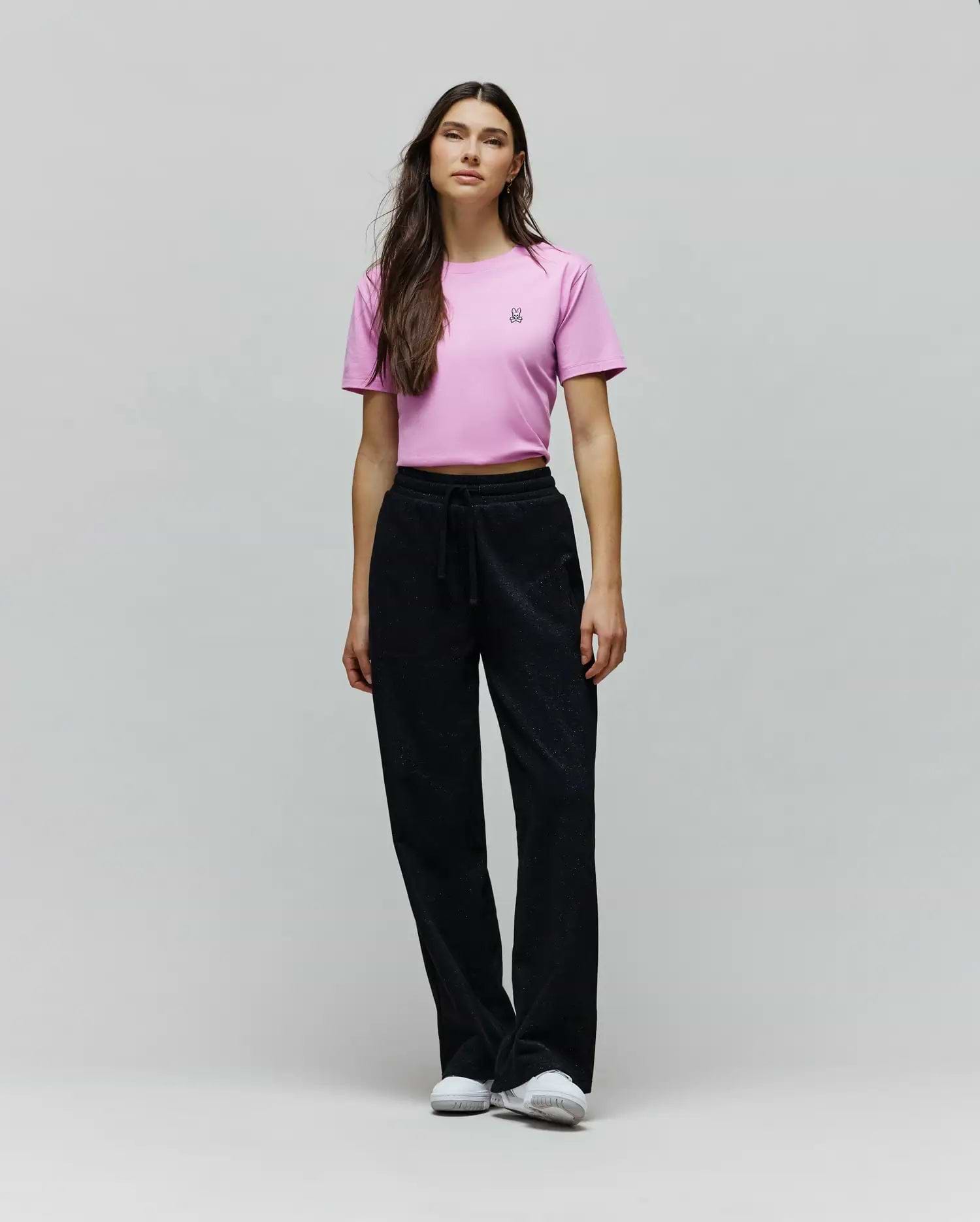 Pink cropped jersey t-shirt with a small embroidered Psycho Bunny skull logo on the left chest, paired with black Womens Jules Lurex Sweatpant featuring a relaxed wide-leg fit and subtle shimmer.