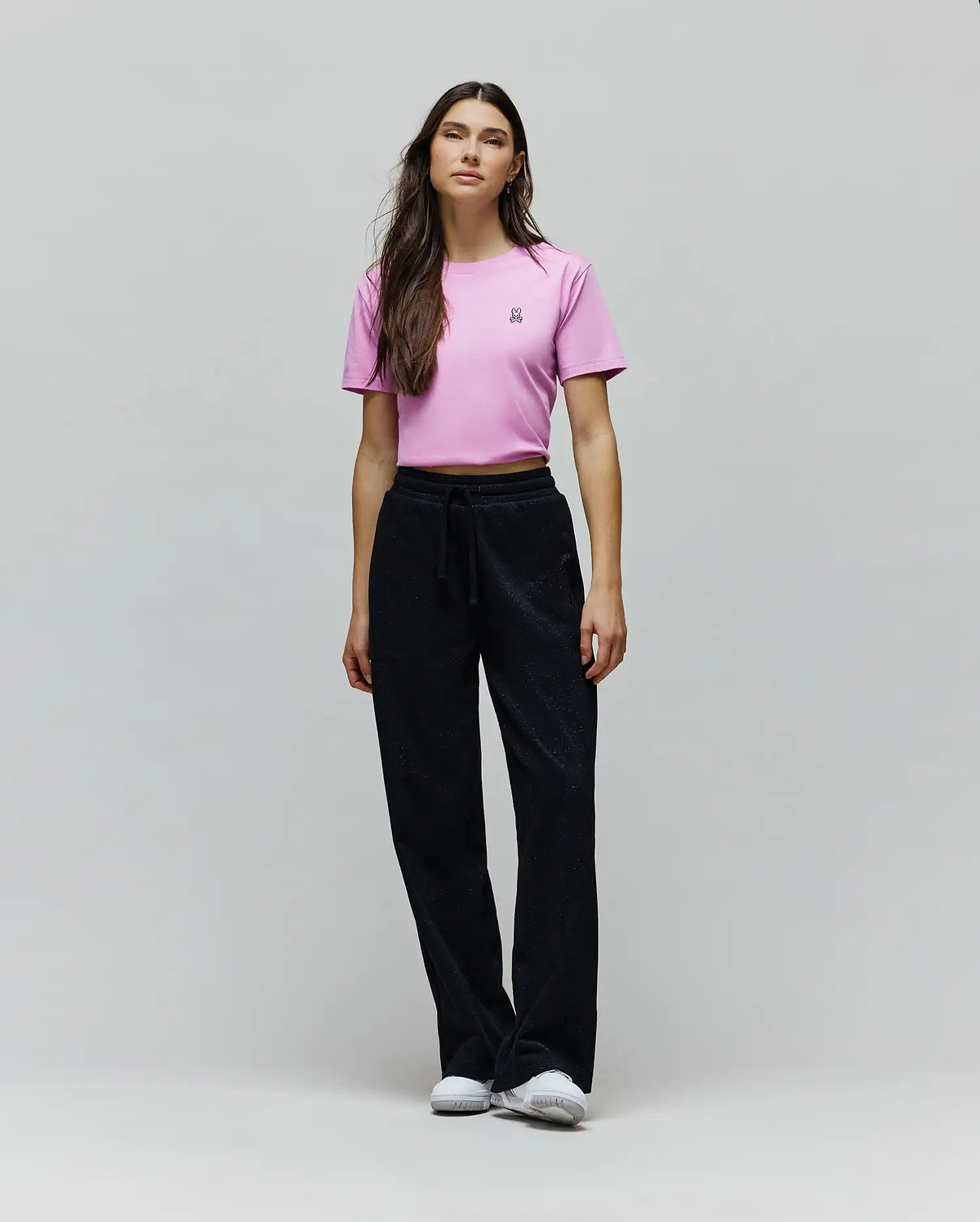 Pink cropped jersey t-shirt with a small embroidered Psycho Bunny skull logo on the left chest, paired with black Womens Jules Lurex Sweatpant featuring a relaxed wide-leg fit and subtle shimmer.
