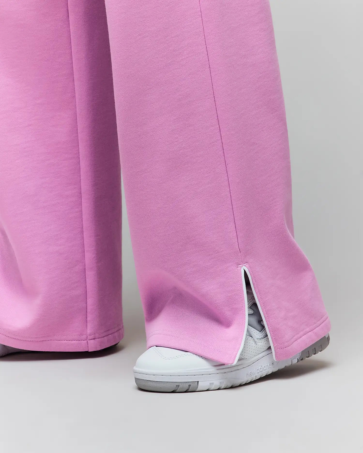 Womens Daisie Fleece Joggers, a relaxed wide-leg style in soft pink fleece jersey, featuring a distinctive ankle split hem with white trim.