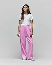 White cropped pique polo with embroidered Psycho Bunny logo, paired with Womens Daisie Fleece Joggers in vibrant pink, featuring a relaxed wide-leg fit and subtle side split detail.