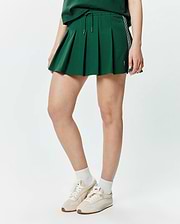 Women's Cecilia Pleated Skort in forest green, featuring a relaxed A-line fit, drawstring waist, white and black side stripes, and a small embroidered Psycho Bunny skull logo. (1)