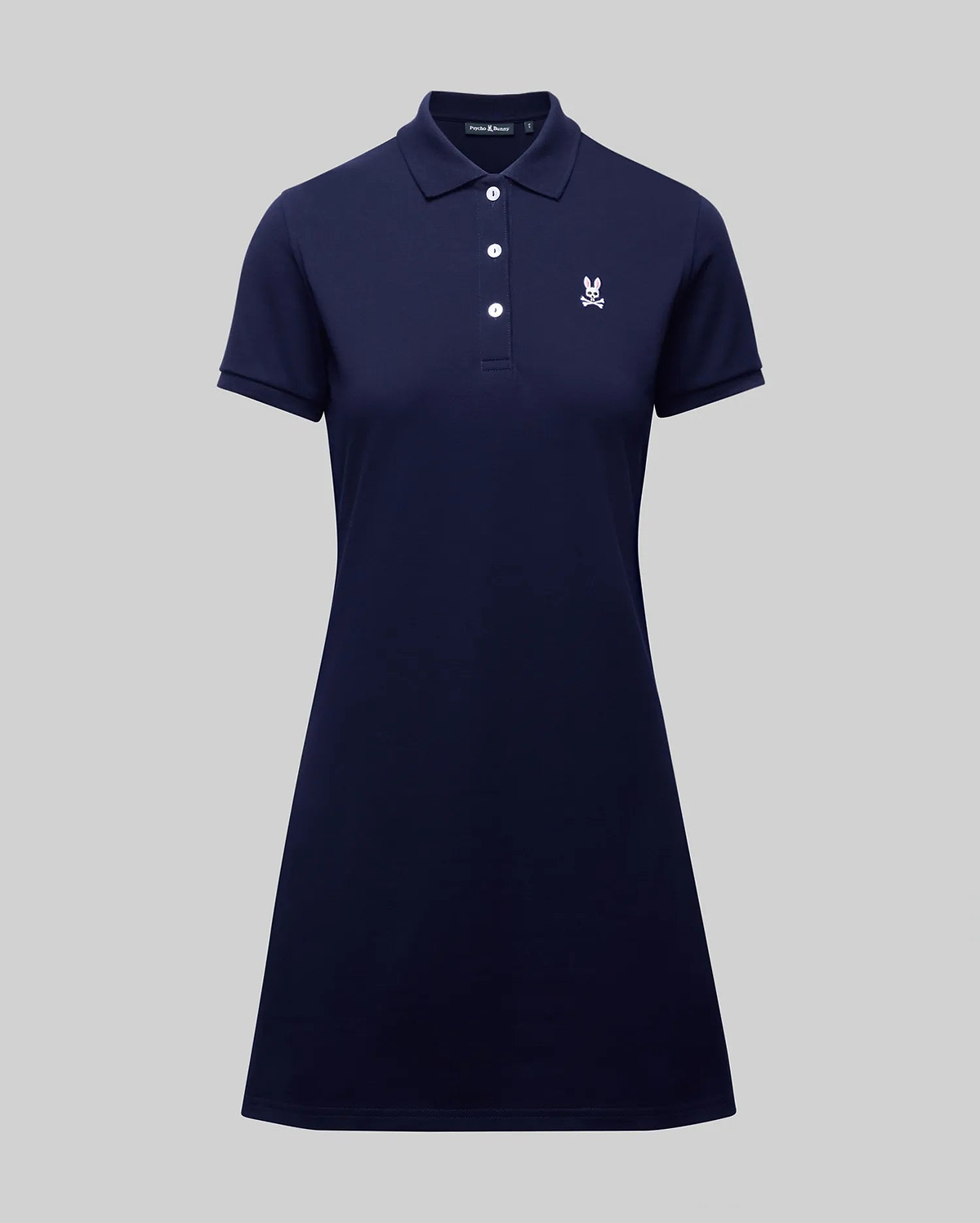 The WOMENS POLO DRESS - WO2000003 by Psycho Bunny is a navy blue, short-sleeve 100% Pima cotton polo dress with a collar, four buttons, white embroidered crest on the chest, and feminine fit. Shown on a plain gray background.