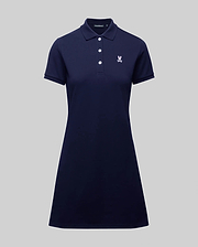 The WOMENS POLO DRESS - WO2000003 by Psycho Bunny is a navy blue, short-sleeve 100% Pima cotton polo dress with a collar, four buttons, white embroidered crest on the chest, and feminine fit. Shown on a plain gray background.