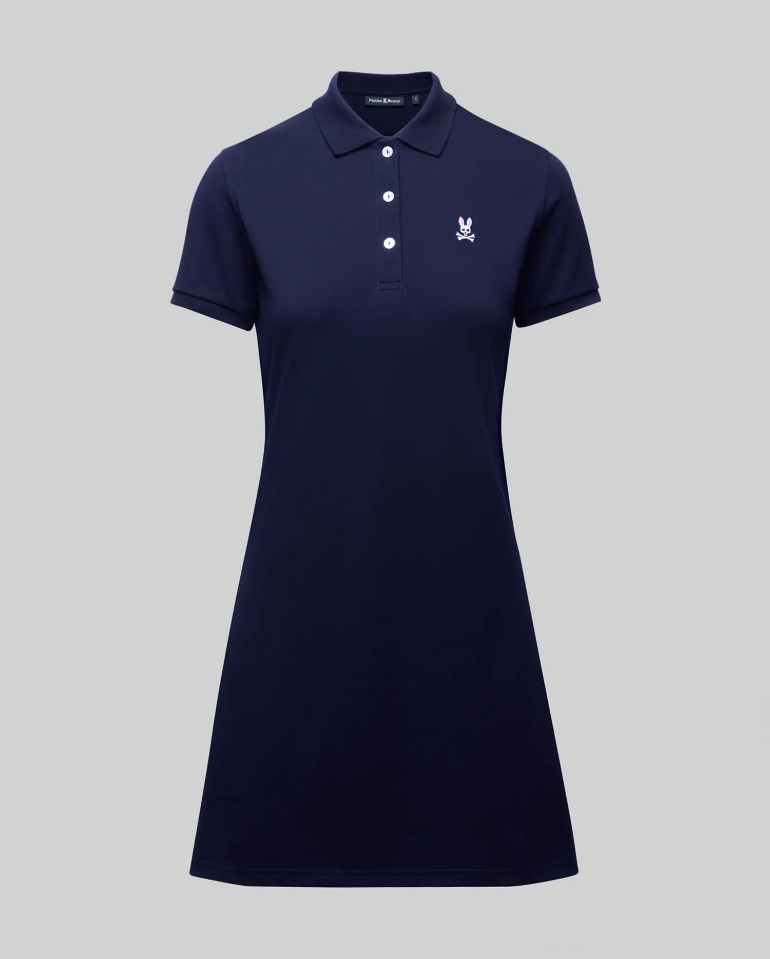 The WOMENS POLO DRESS - WO2000003 by Psycho Bunny is a navy blue, short-sleeve 100% Pima cotton polo dress with a collar, four buttons, white embroidered crest on the chest, and feminine fit. Shown on a plain gray background.