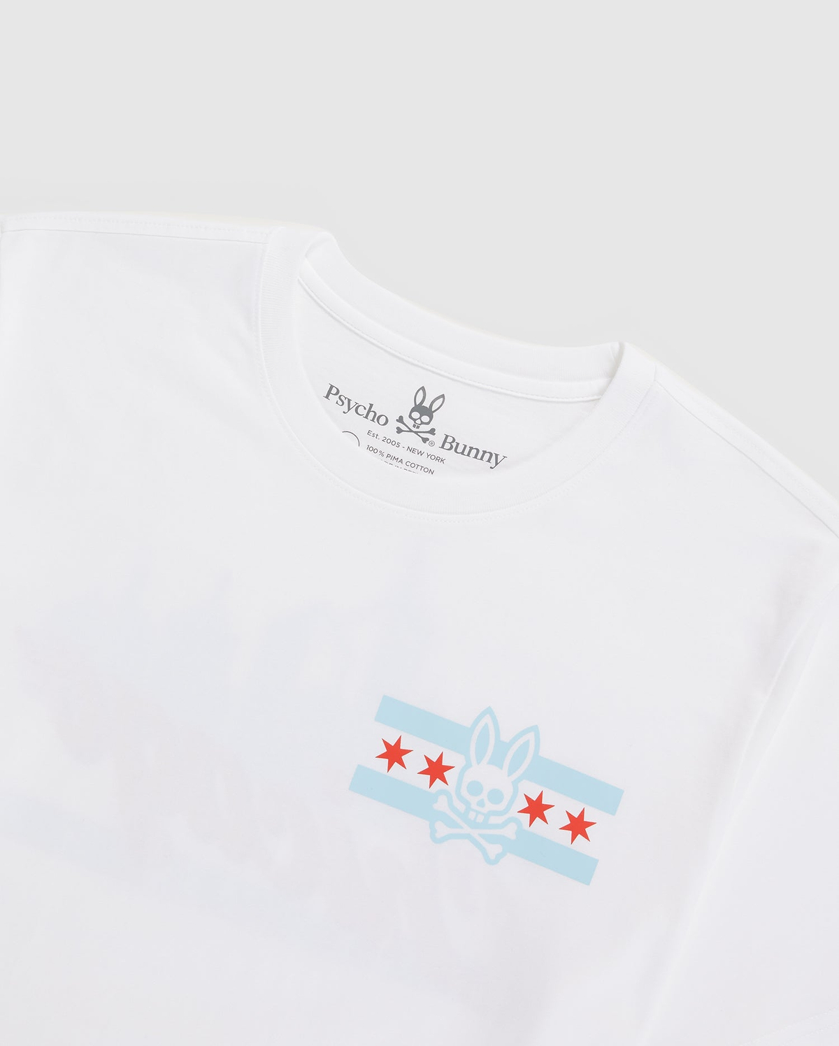 The MENS CHICAGO CITY TEE - B6U551W1PC by Psycho Bunny is made from soft Pima cotton jersey and features a faded city skyline along with their signature bunny logo, inspired by the Chicago flag. The design includes red stars, light blue stripes, and "Psycho Bunny" on the inside label.