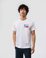 A young man with curly hair wearing a white MENS TEXAS TEE - B6U553W1PC shirt with a "Psycho Bunny" logo on the chest, paired with dark pants, standing against a plain background.