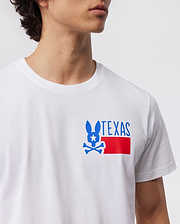 A person is wearing a Psyco Bunny MENS TEXAS TEE - B6U553W1PC, crafted from Pima cotton. The white t-shirt features a blue silhouette of a rabbit with a skull and crossbones underneath, a white star on the rabbit's head, and the word "TEXAS" in blue text. A red rectangle is positioned beneath the design. Only the torso and part of the face are visible.