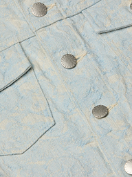 Close-up of the Maven Jacket in light blue textured cotton jacquard, showcasing a subtle floral pattern, two silver metal buttons, and part of a flap pocket for a structured look.