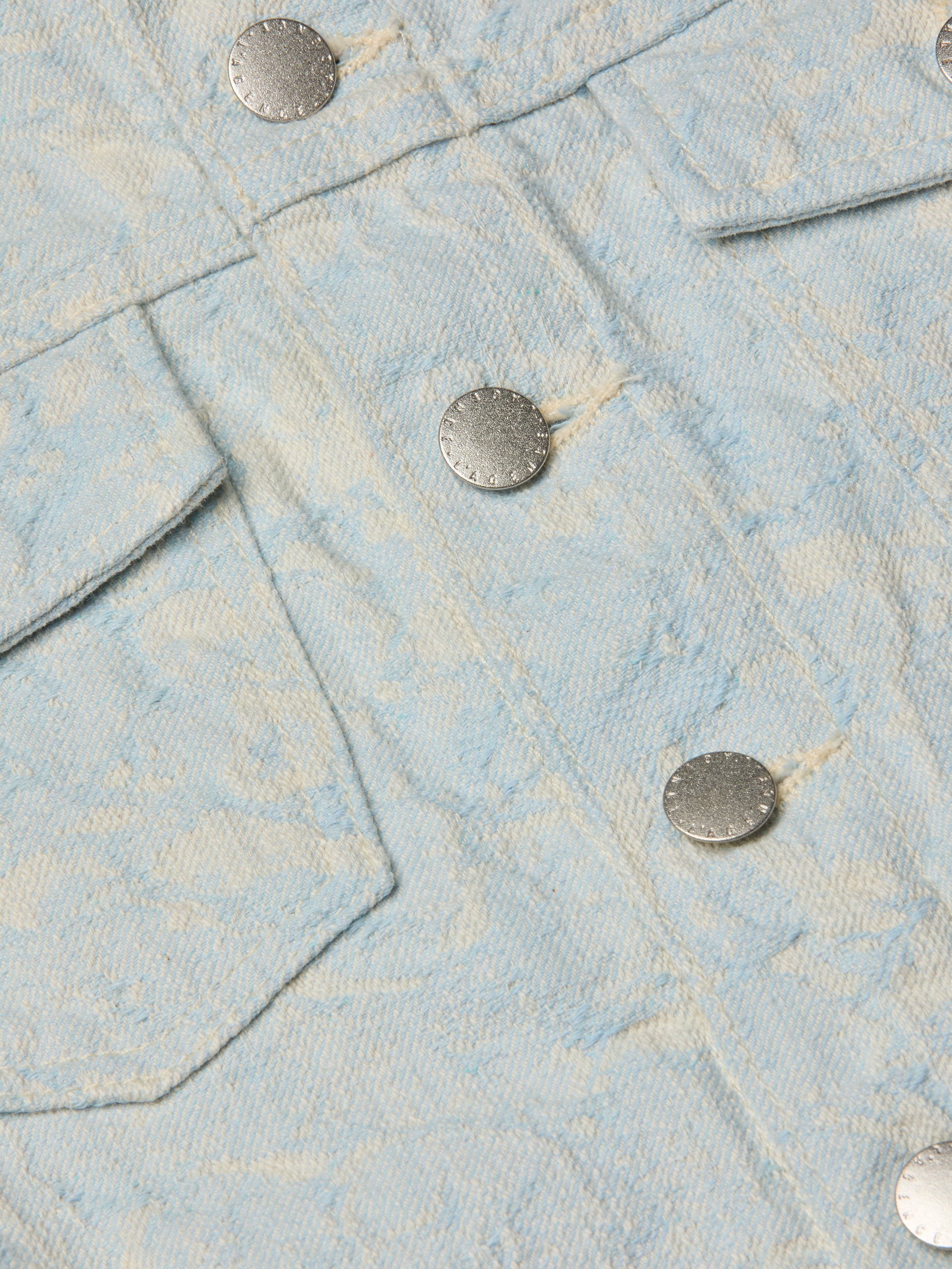 Close-up of the Maven Jacket in light blue textured cotton jacquard, showcasing a subtle floral pattern, two silver metal buttons, and part of a flap pocket for a structured look.