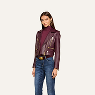 A woman wearing the Blakely Leather Biker Jacket in burgundy over a matching turtleneck and blue jeans stands against a plain light background.