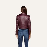 A person with long brown hair is shown from behind, wearing the Blakely Leather Biker Jacket in burgundy lambskin leather with a cropped fit and blue jeans, standing against a plain light background.