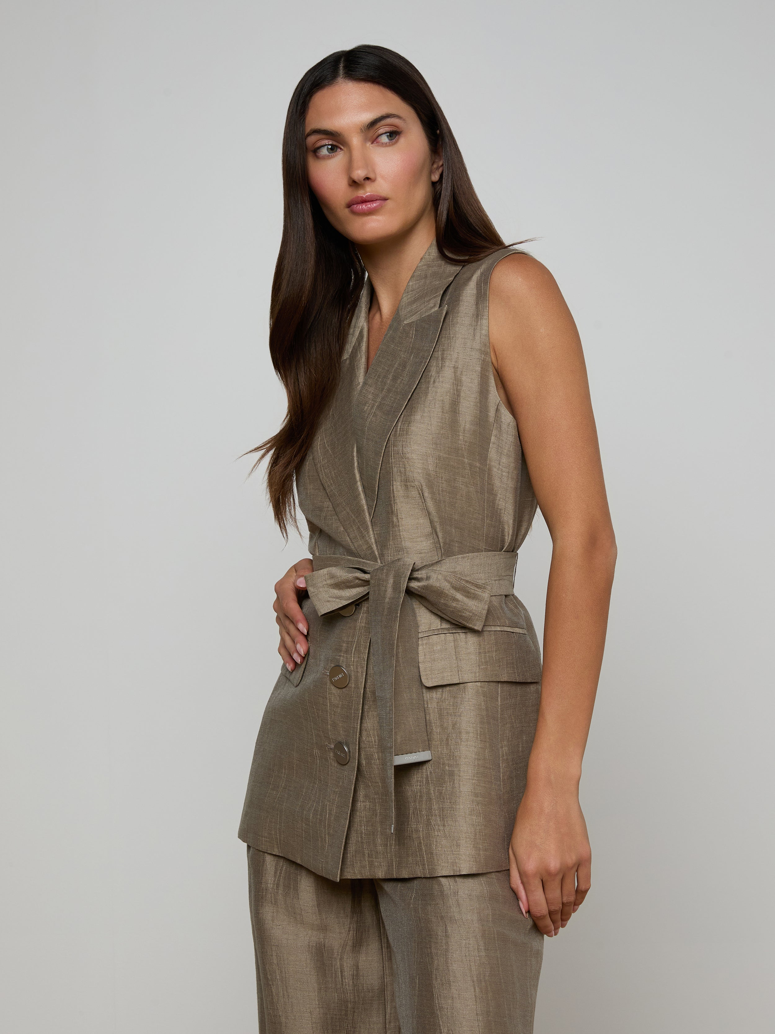 A woman with long dark hair wears the Harper Linen-Blend Vest with a tie belt and matching pants, standing against a plain off-white background and looking slightly to the side.