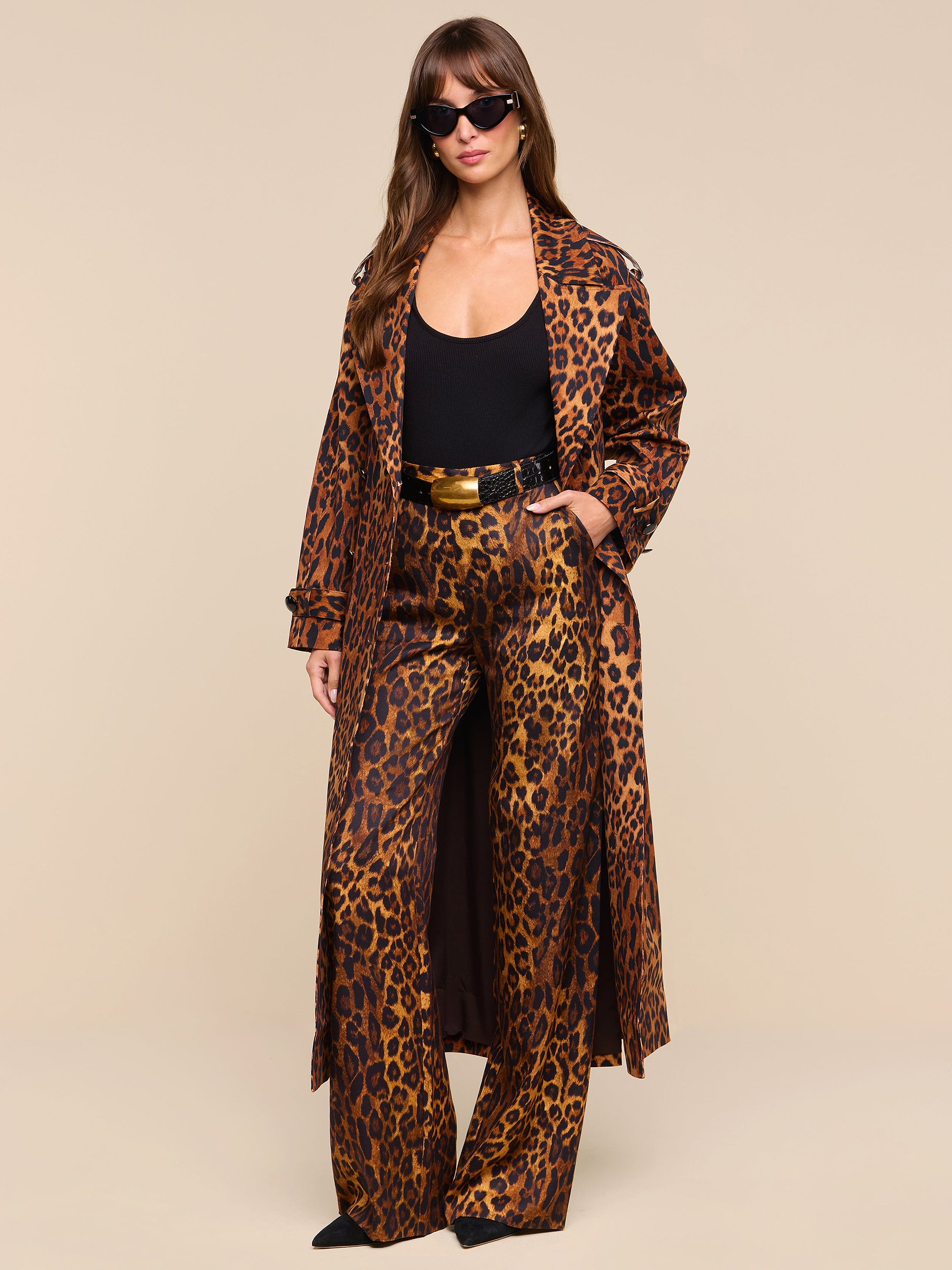 A woman wearing sunglasses, a black top, and the Brinley Oversized Trench Coat in a bold leopard print stands confidently against a plain white background.