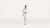 A person wearing a white jacket, white top, and white pants walks forward against a plain white background.