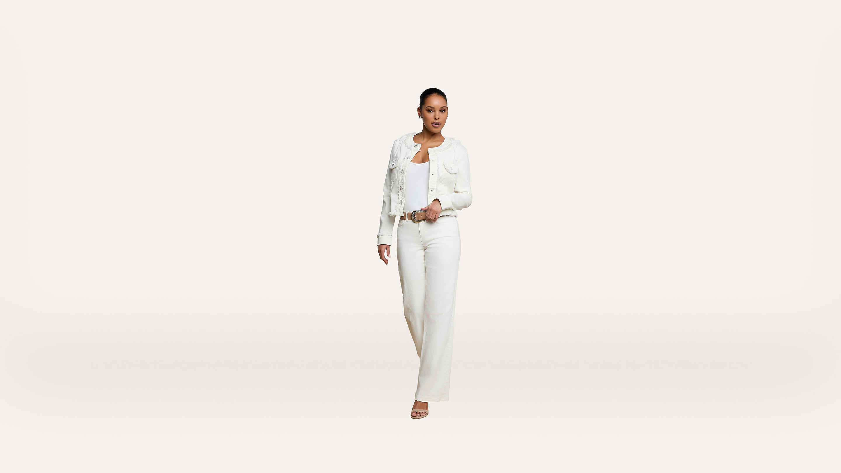 A person wearing a white jacket, white top, and white pants walks forward against a plain white background.
