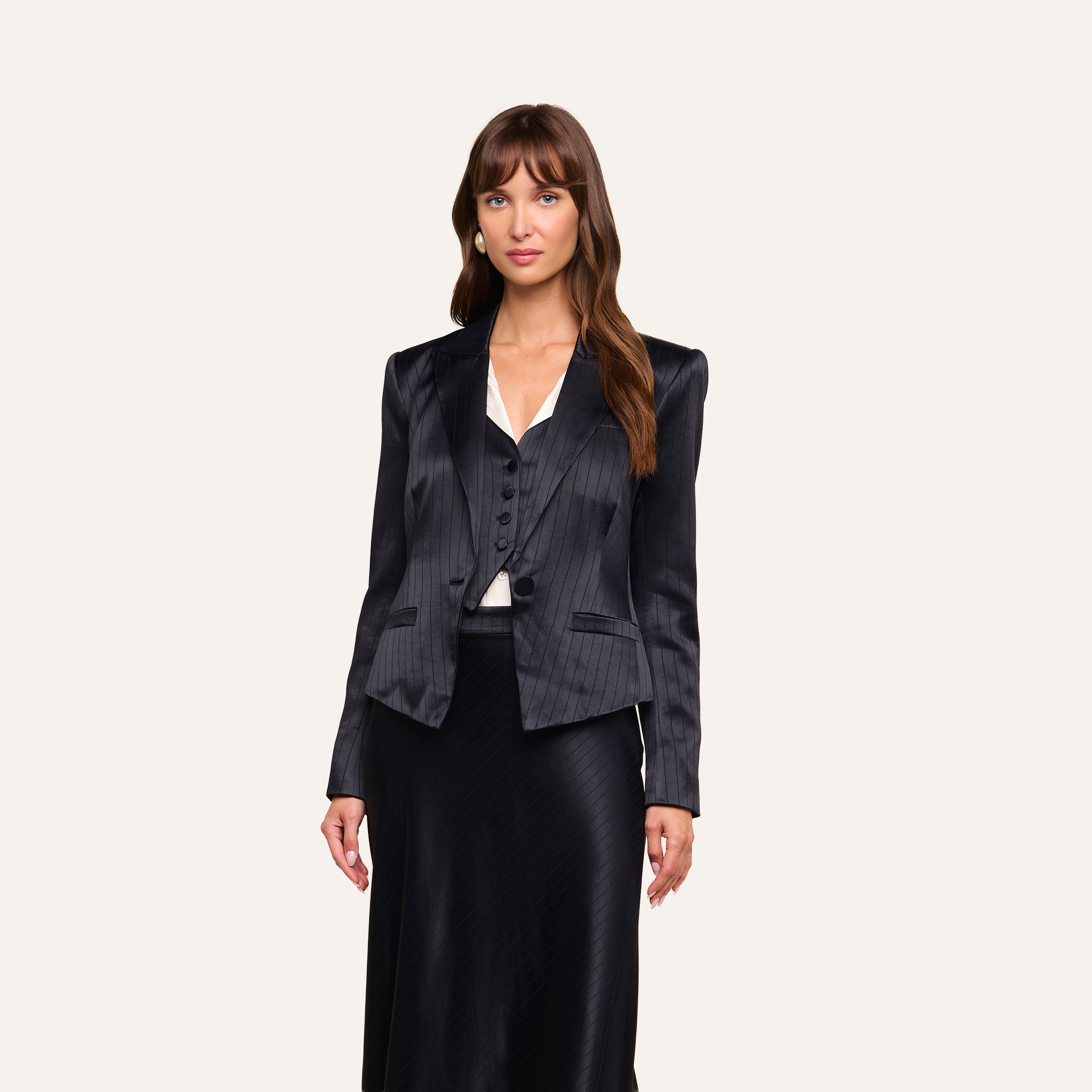A woman with long brown hair wears the Misa Blazer, paired with a matching vest and black skirt, standing against a plain light background. She faces forward with a neutral expression.