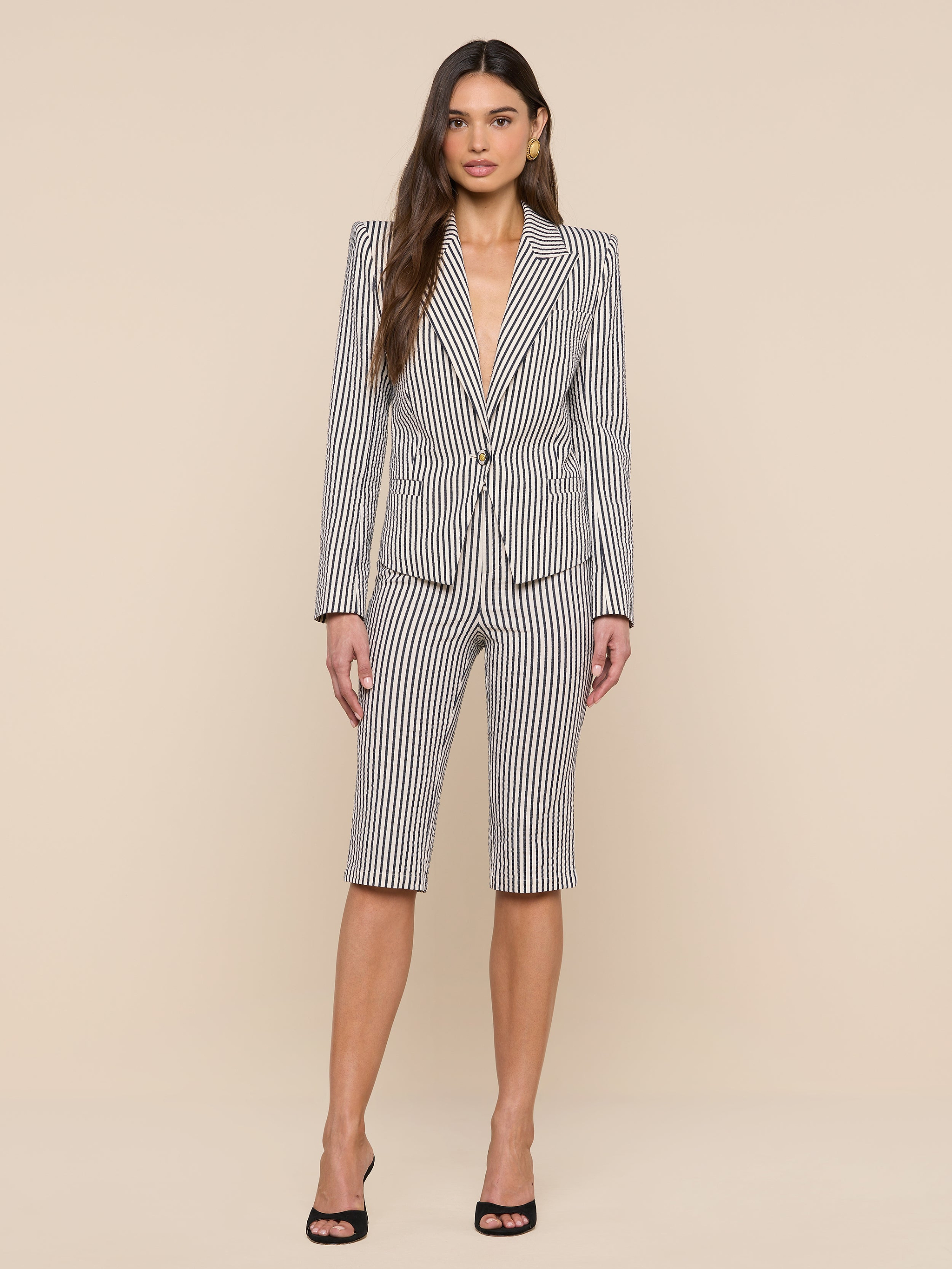 A woman stands facing forward wearing the Misa Seersucker Blazer, styled with matching gray striped knee-length shorts and black high heels against a plain white background.