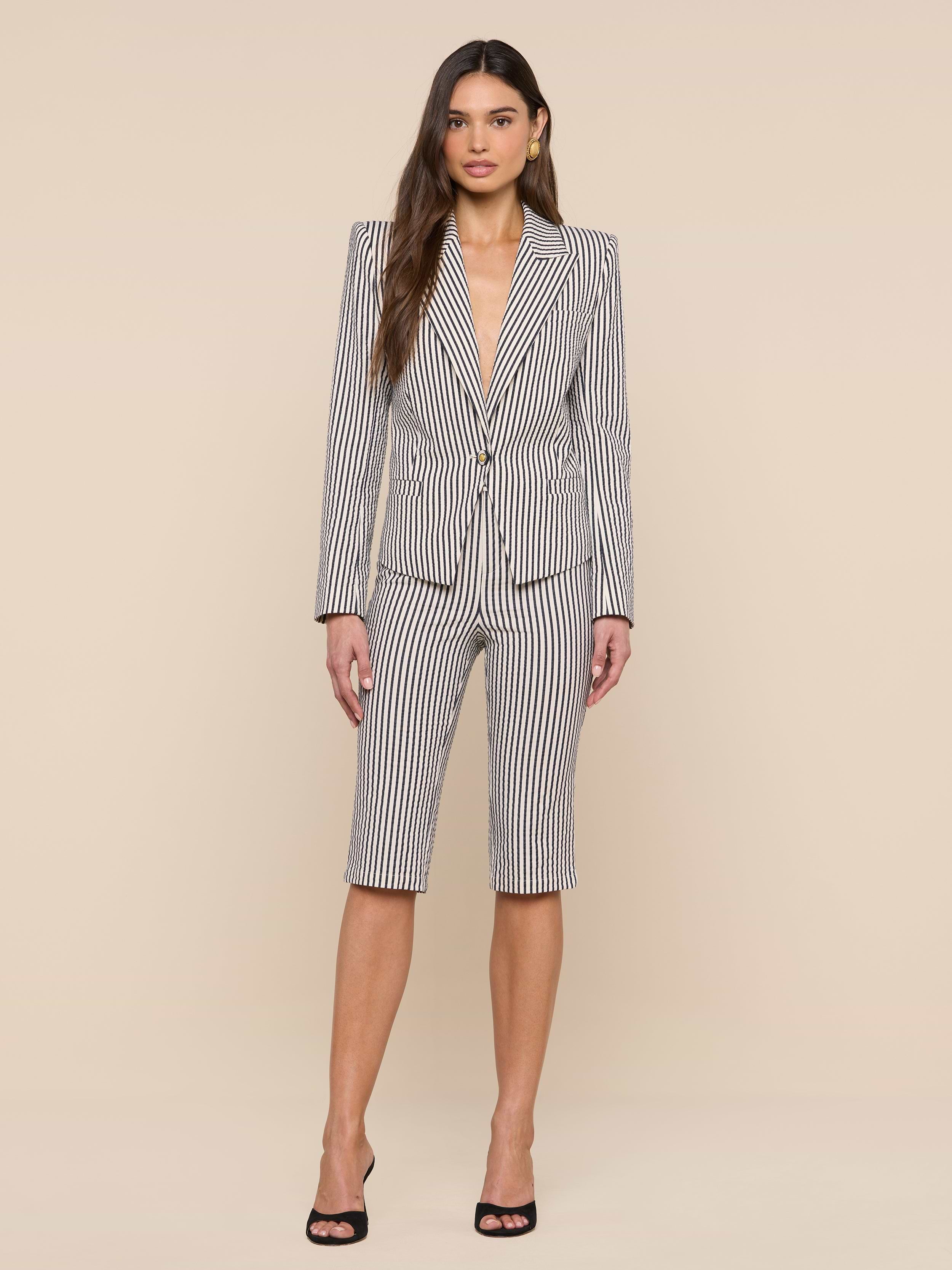 A woman stands facing forward wearing the Misa Seersucker Blazer, styled with matching gray striped knee-length shorts and black high heels against a plain white background.