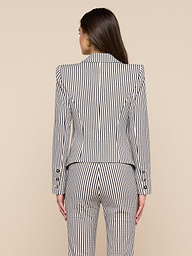 A woman with long brown hair is shown from behind, wearing the Misa Seersucker Blazer with matching pants against a plain light background.