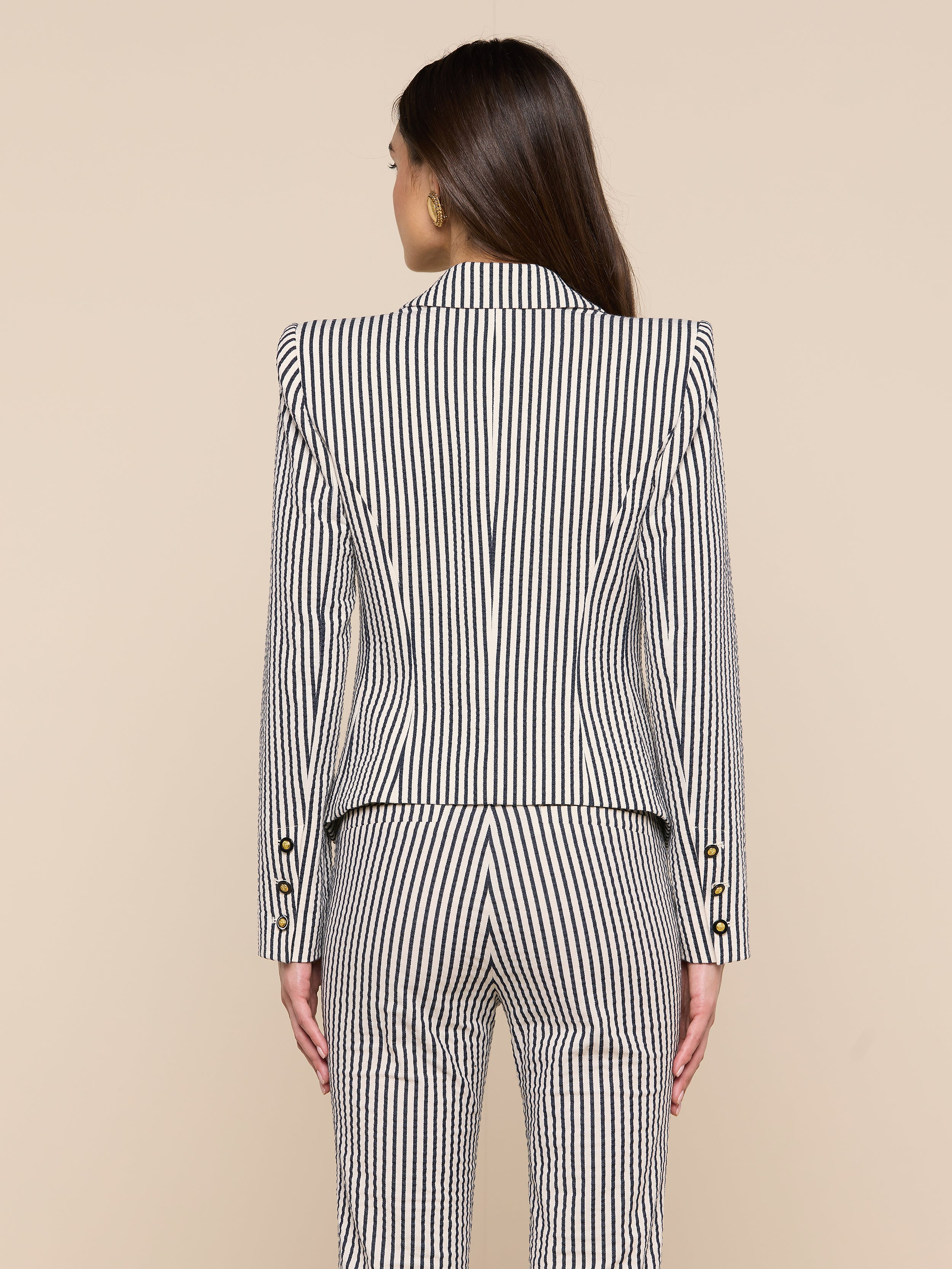 A woman with long brown hair is shown from behind, wearing the Misa Seersucker Blazer with matching pants against a plain light background.