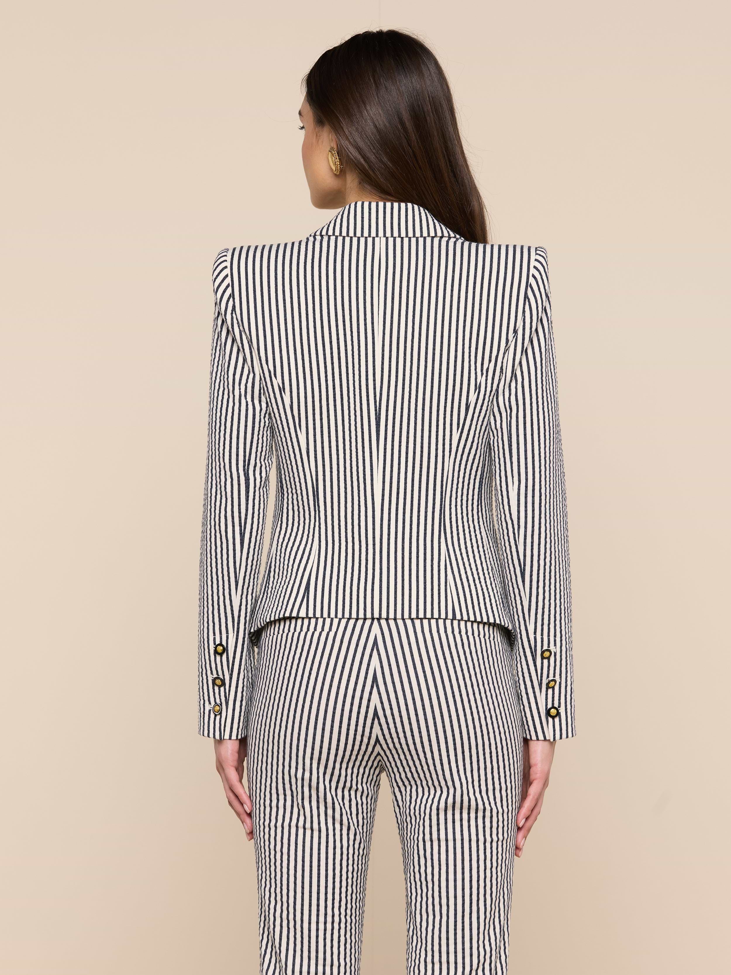 A woman with long brown hair is shown from behind, wearing the Misa Seersucker Blazer with matching pants against a plain light background.