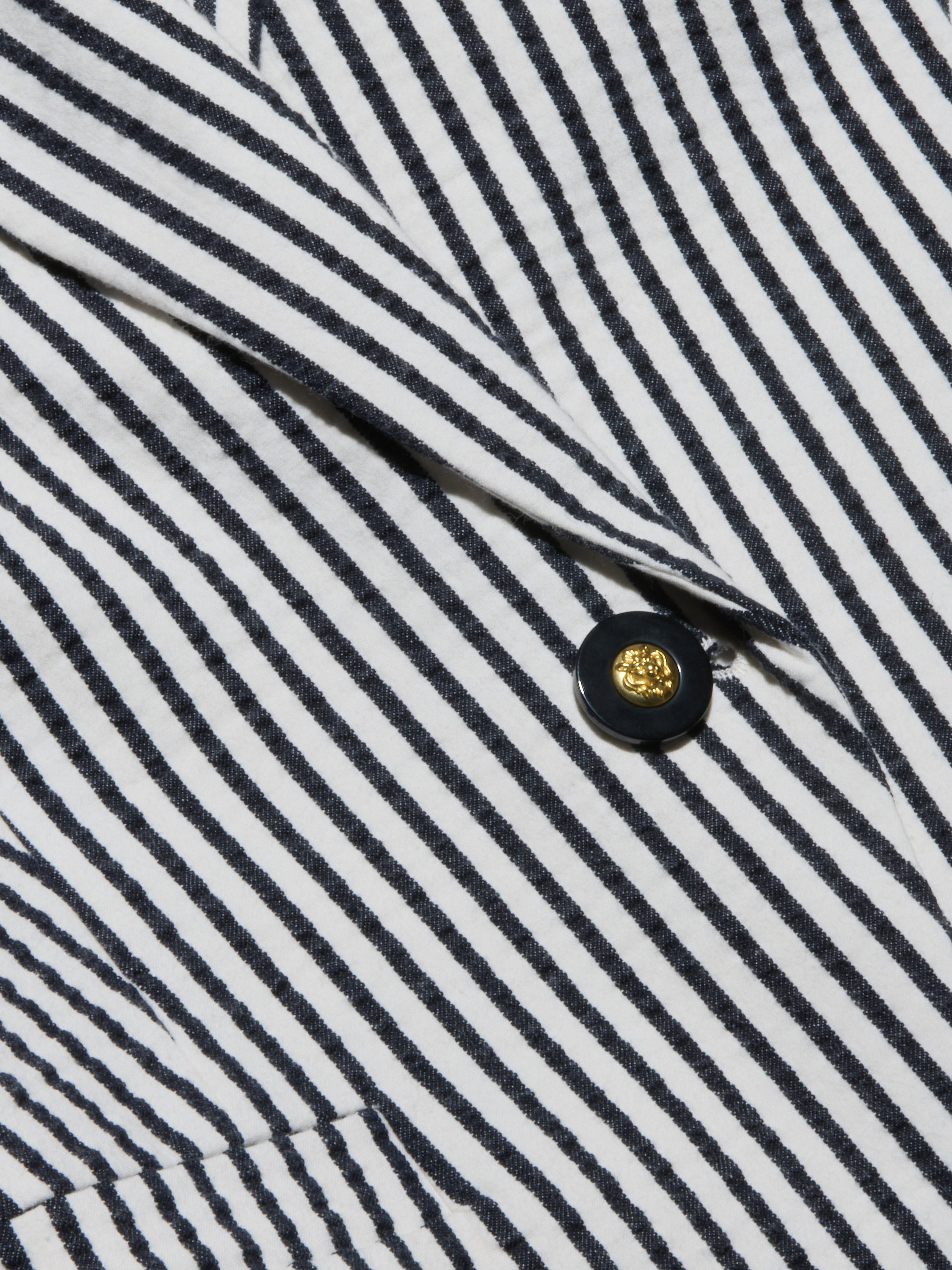 Close-up of the Misa Seersucker Blazer fabric, featuring black and white diagonal stripes and a gold button with a shiny center encircled by a black rim.