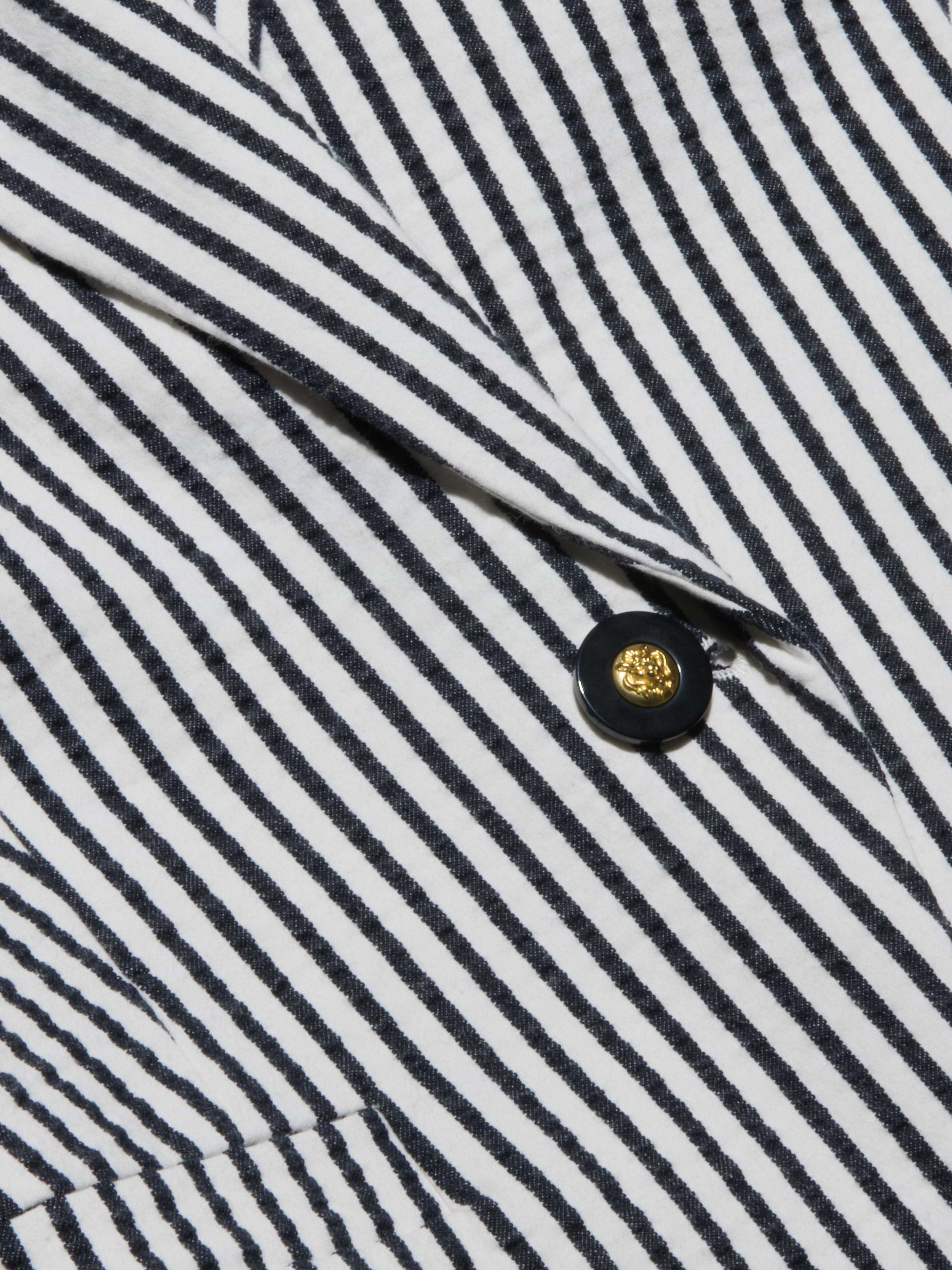 Close-up of the Misa Seersucker Blazer fabric, featuring black and white diagonal stripes and a gold button with a shiny center encircled by a black rim.