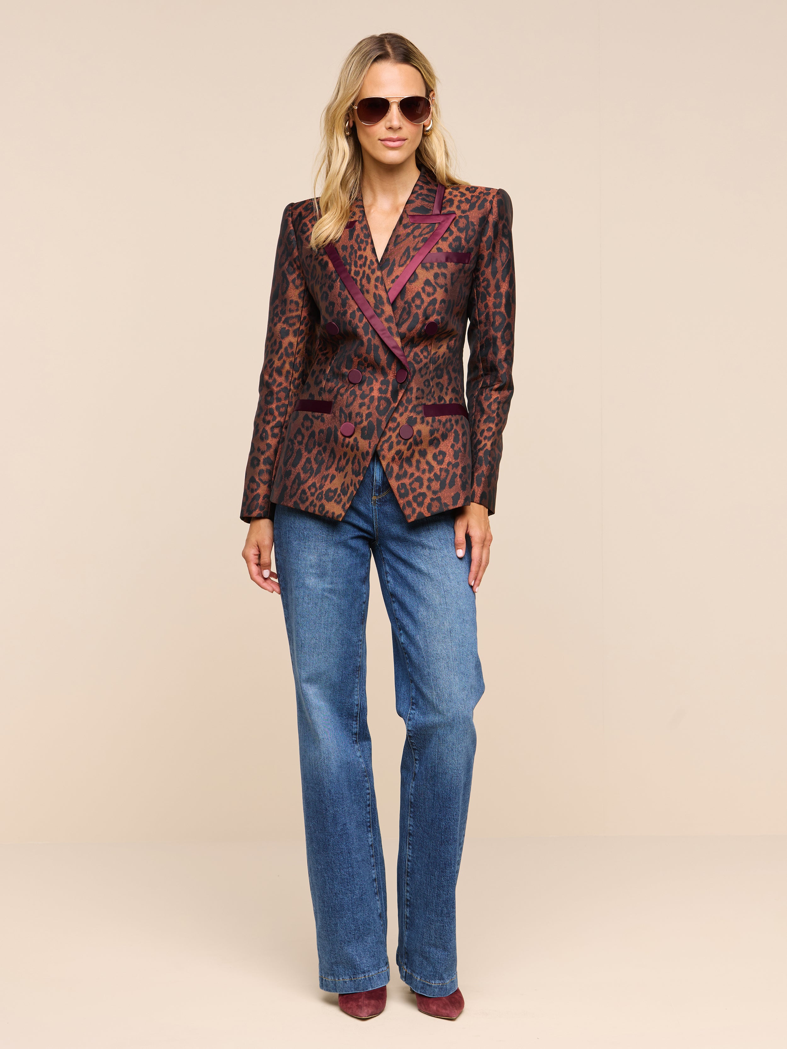 A woman wearing sunglasses, blue jeans, pointed shoes, and the Kyomi Double-Breasted Blazer stands against a plain white background.