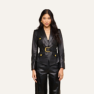 A woman stands facing forward against a plain light background, wearing the Wisteria Leather Blazer—a fitted black leather blazer with gold buttons and a belt—paired with matching black leather pants.