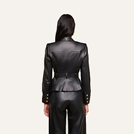 A woman with long dark hair, seen from behind, wears the fitted Wisteria Leather Blazer in black, paired with matching pants. The blazer features gold buttons on the cuffs and a belted waist. The background is plain and light-colored.