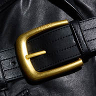 A close-up of a shiny gold belt buckle engraved with the word LAGENCE adorns a black leather belt set against the luxurious black leather background of the Wisteria Leather Blazer, evoking sophisticated, tailored style.