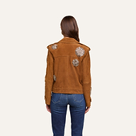 A person with long brown hair, wearing blue jeans and the Xoey Cropped Crystal Trench Coat—featuring decorative white floral patterns—is standing facing away from the camera against a plain light background, in a look inspired by Fall 2026 Fashion Week.