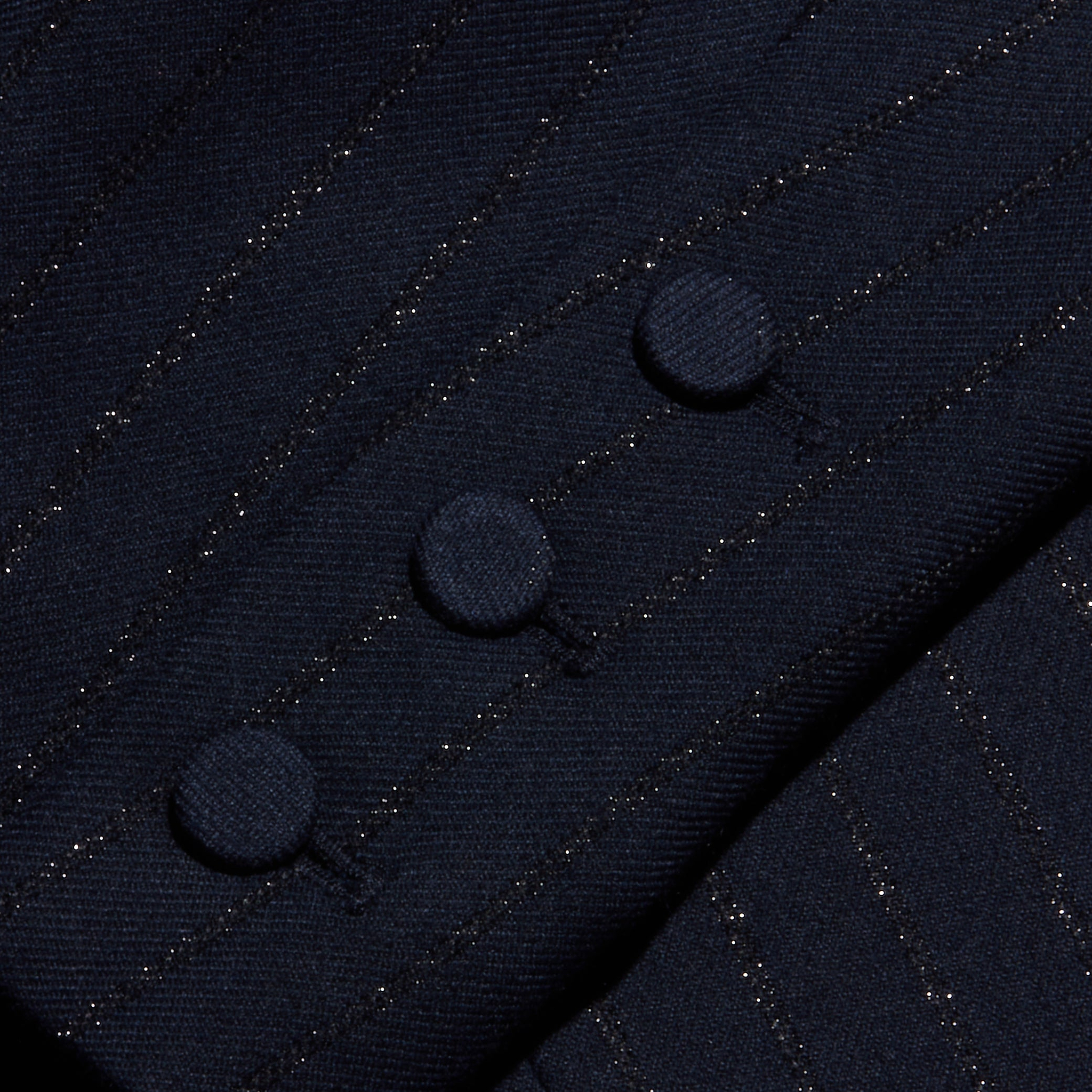 Close-up of the Risa Double-Breasted Blazer sleeve featuring three fabric-covered buttons in a row, highlighting the fine texture and subtle shimmer of Lurex woven into its dark pinstripe material.