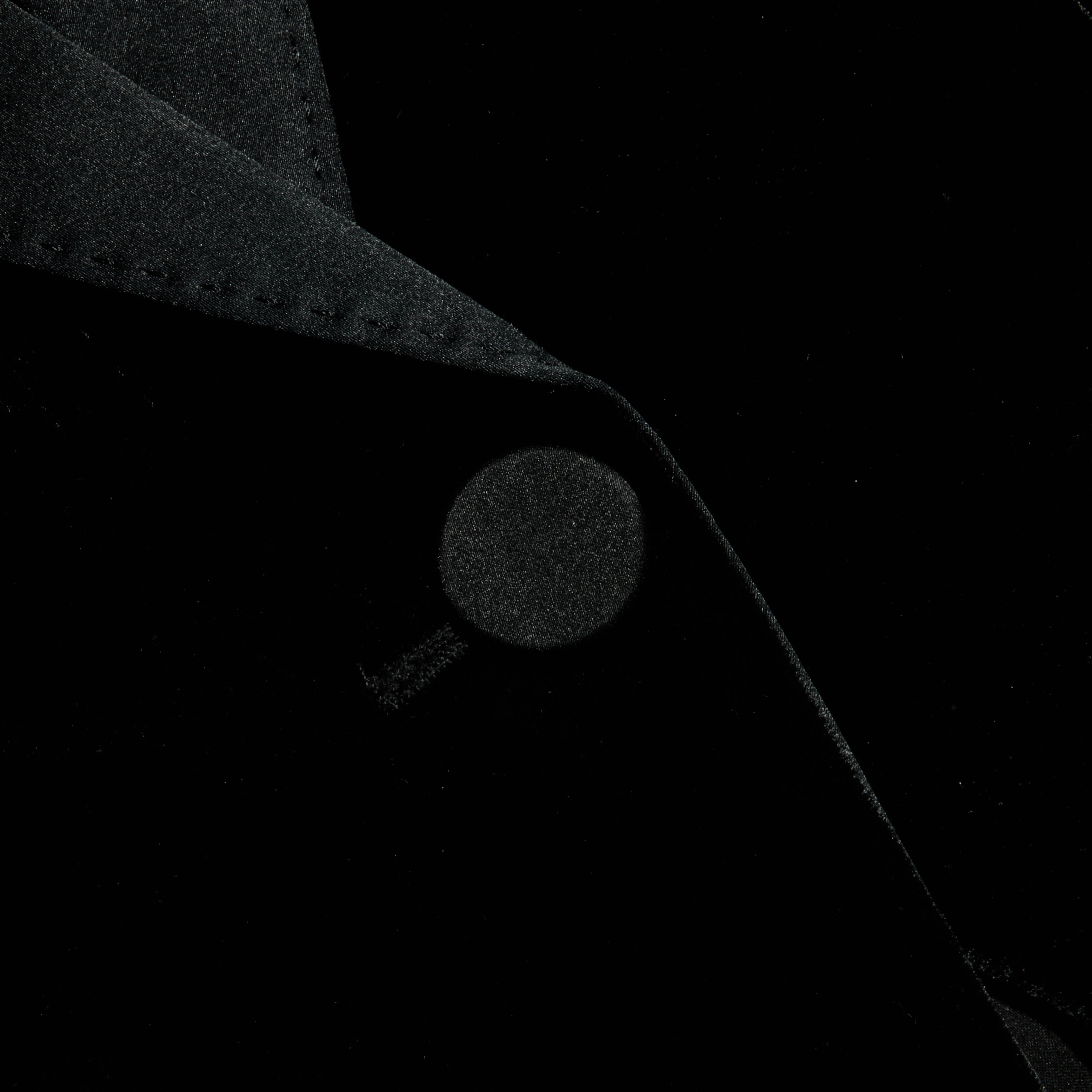 A close-up of the Philippa Velvet Blazer showcases the collar and a button, emphasizing the rich texture and folds of its black velvet fabric, while satin lapels add an elegant touch.