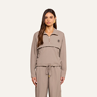 A woman with long brown hair wears the Vex Cropped Windbreaker in taupe, paired with matching drawstring pants, standing against a plain light background and looking directly at the camera with a neutral expression.