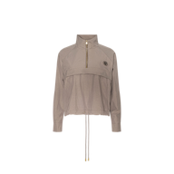 Vex Cropped Windbreaker in light brown, featuring long sleeves, a half-zip front, high collar, drawstring hem, and a small round emblem on the left chest, displayed on a plain white background.