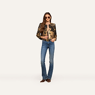 Wearing sunglasses, a person stands against a plain white background dressed in the Lian Tapestry Jacket, paired with a light brown top, blue jeans, and brown shoes.