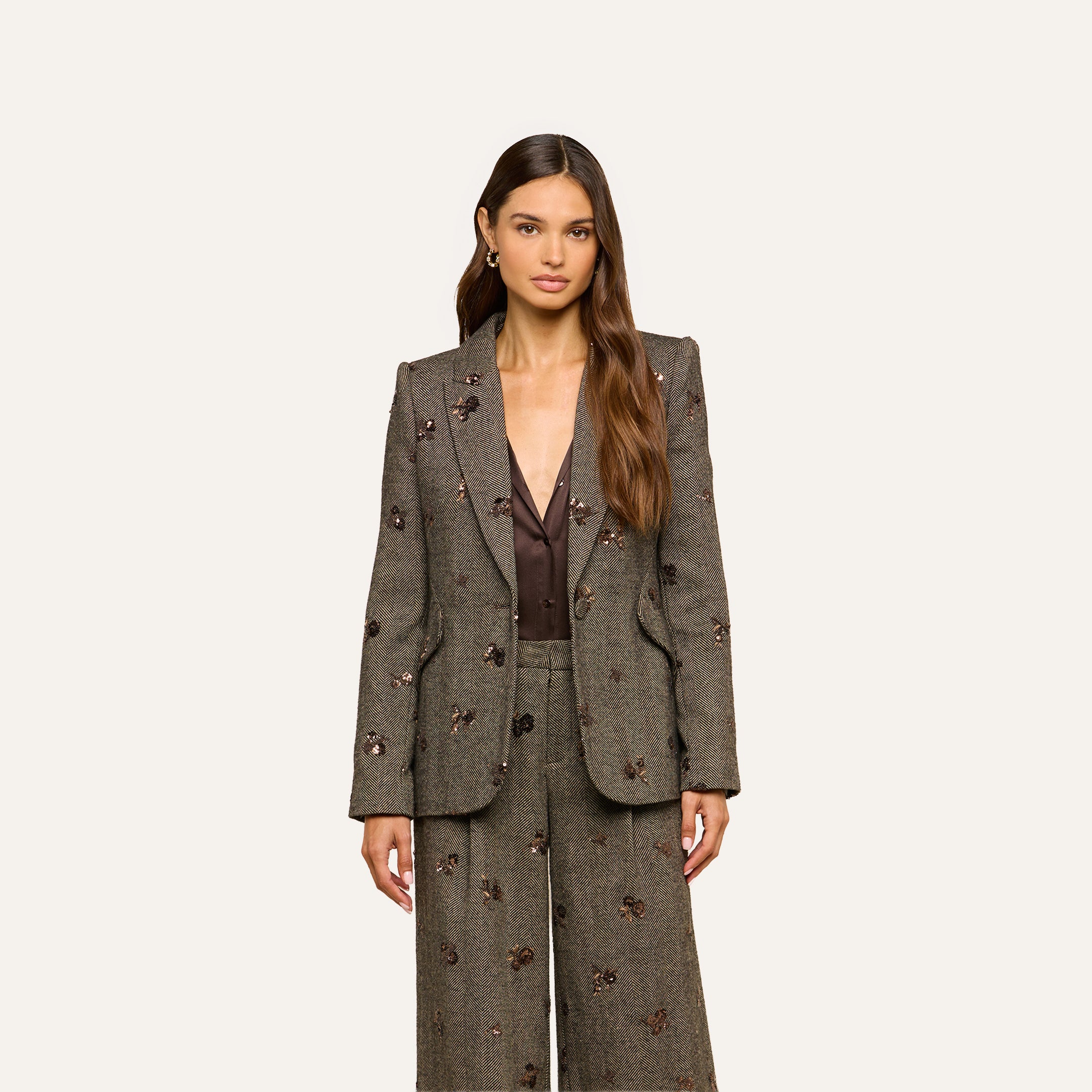A woman with long brown hair wears the Chamberlain Sequined Blazer over a deep brown top, paired with matching pants. She stands against a plain, light background, facing forward with a neutral expression.