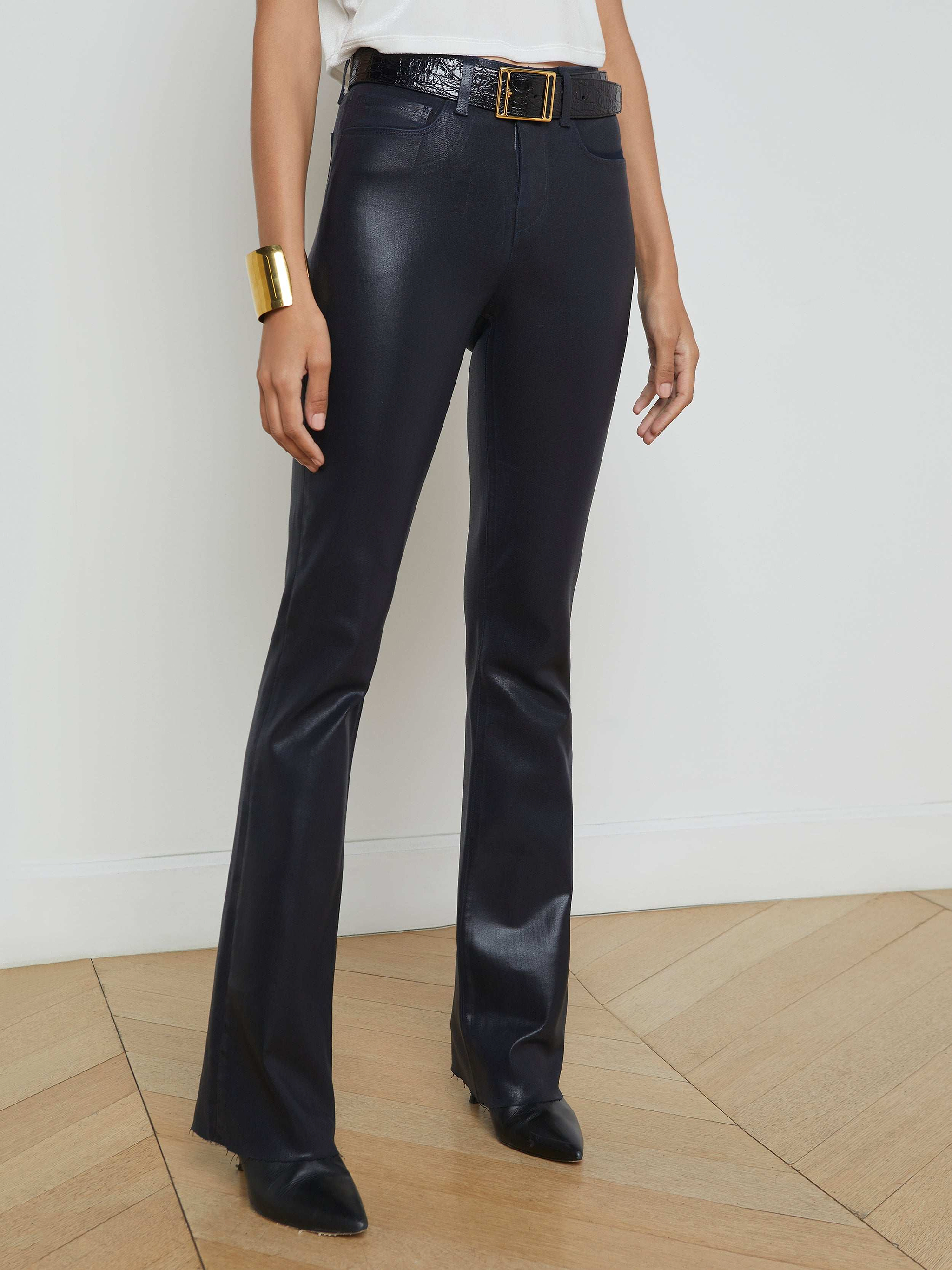 A person wearing the Ruth Coated Straight-Leg Jean with a belt and black shoes, paired with a white top and gold bracelet, stands against a plain light background.