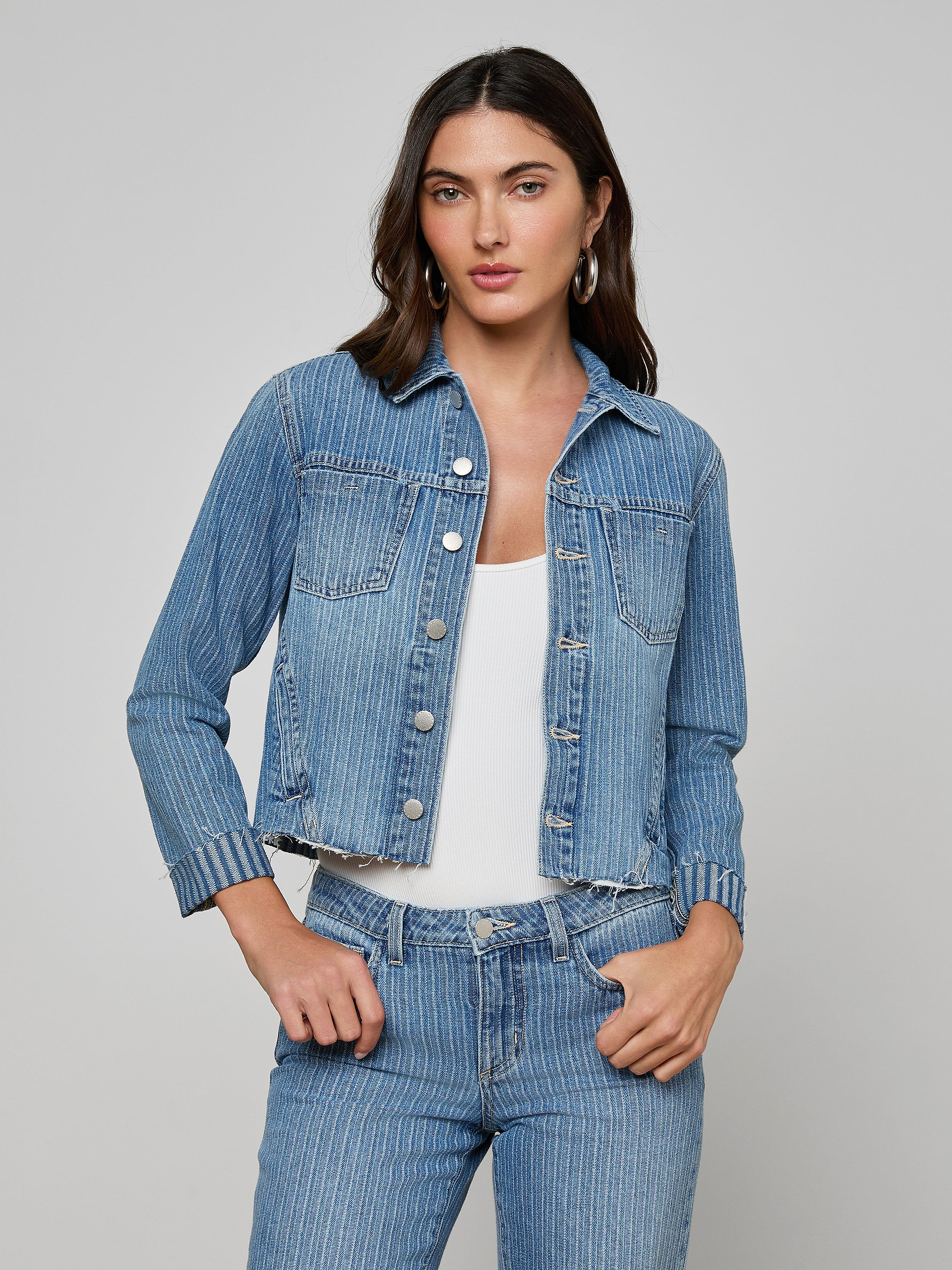 A woman wears the slim-fit Janelle Jean Jacket in all-cotton pinstriped indigo over a white top, paired with matching pinstriped jeans, standing against a plain light background.