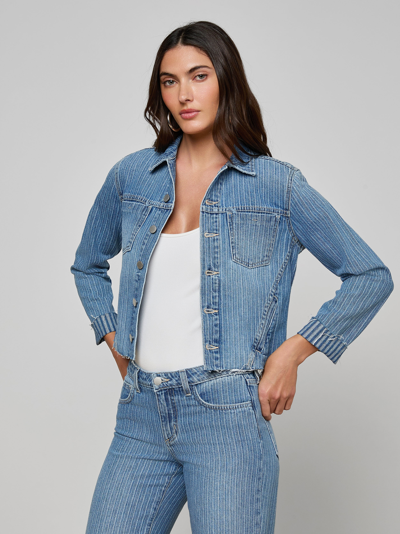 A woman stands with her hands in her pockets, wearing the slim fit Janelle Jean Jacket and matching all-cotton denim jeans over a white top, looking forward against a plain light background.