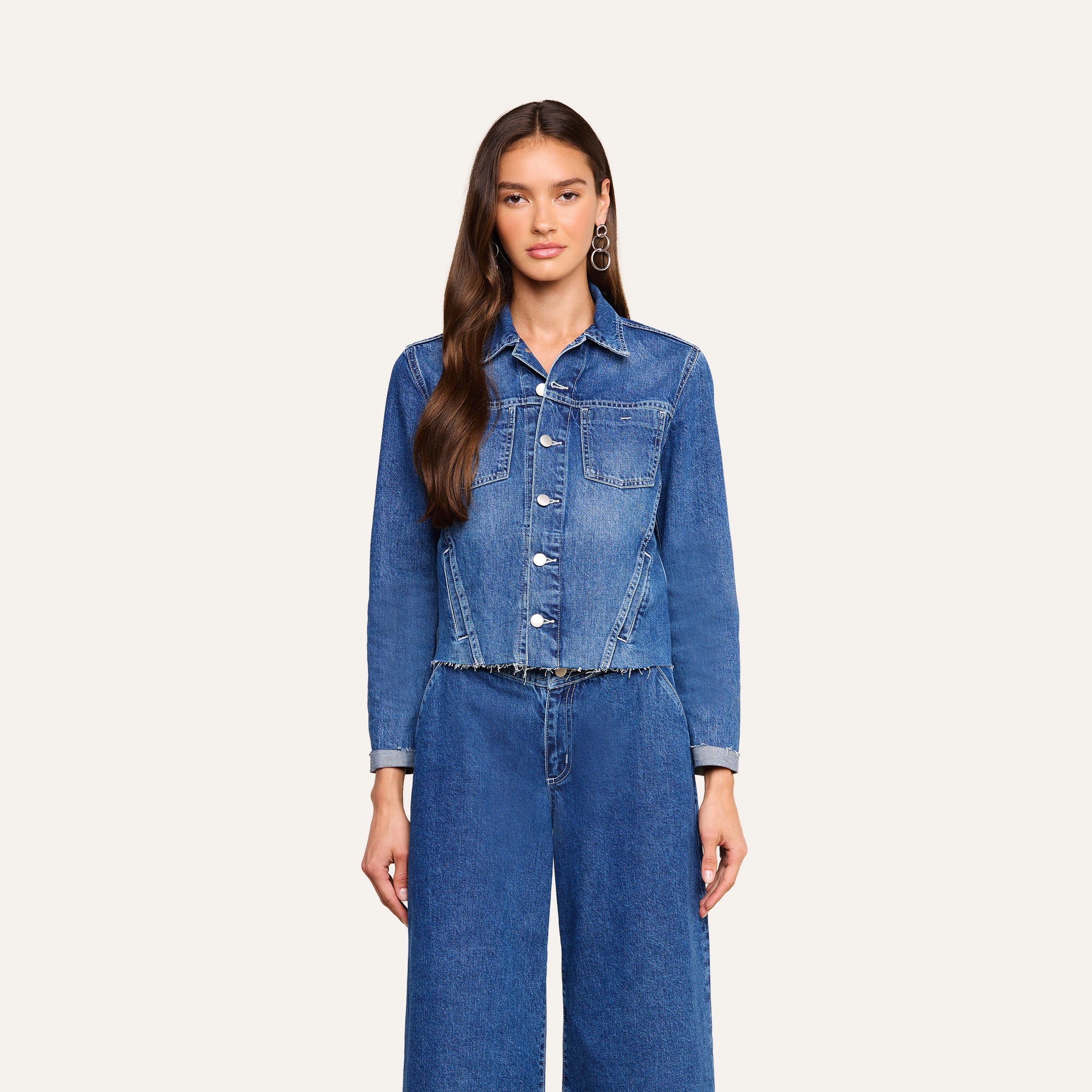 A woman with long brown hair wears the Janelle Jean Jacket in a medium wash with button closure, paired with matching wide-leg blue jeans, standing against a plain light background.