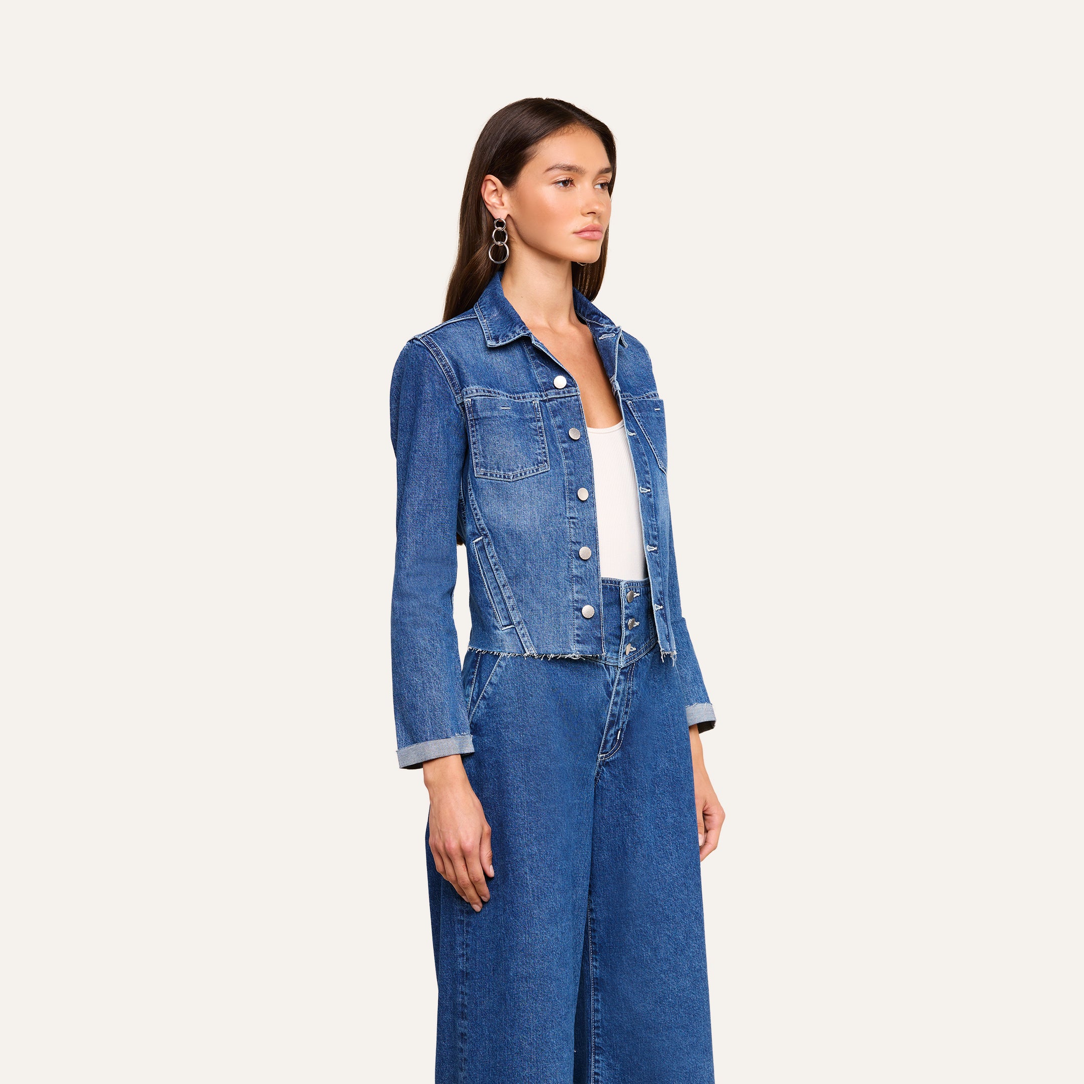 Wearing the Janelle Jean Jacket over a white top and matching high-waisted slim fit denim pants, a woman stands against a plain light background.