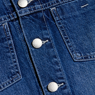 Close-up of the Janelle Jean Jacket in a blue medium wash, featuring silver metal buttons, visible stitching, and portions of two front pockets.