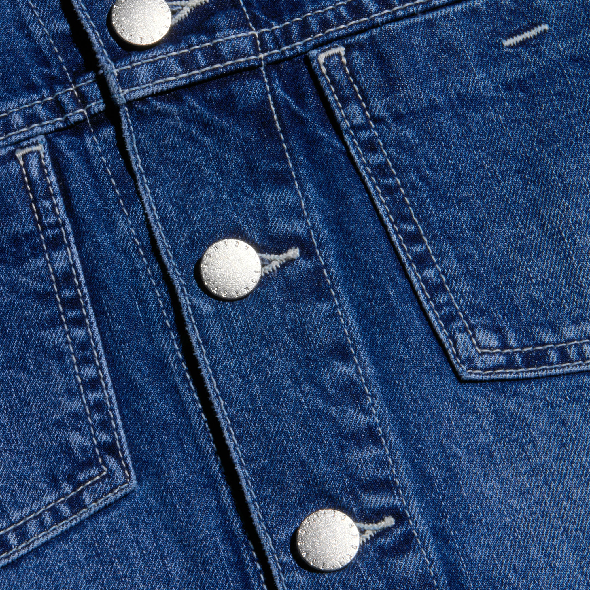 Close-up of the Janelle Jean Jacket in a blue medium wash, featuring silver metal buttons, visible stitching, and portions of two front pockets.