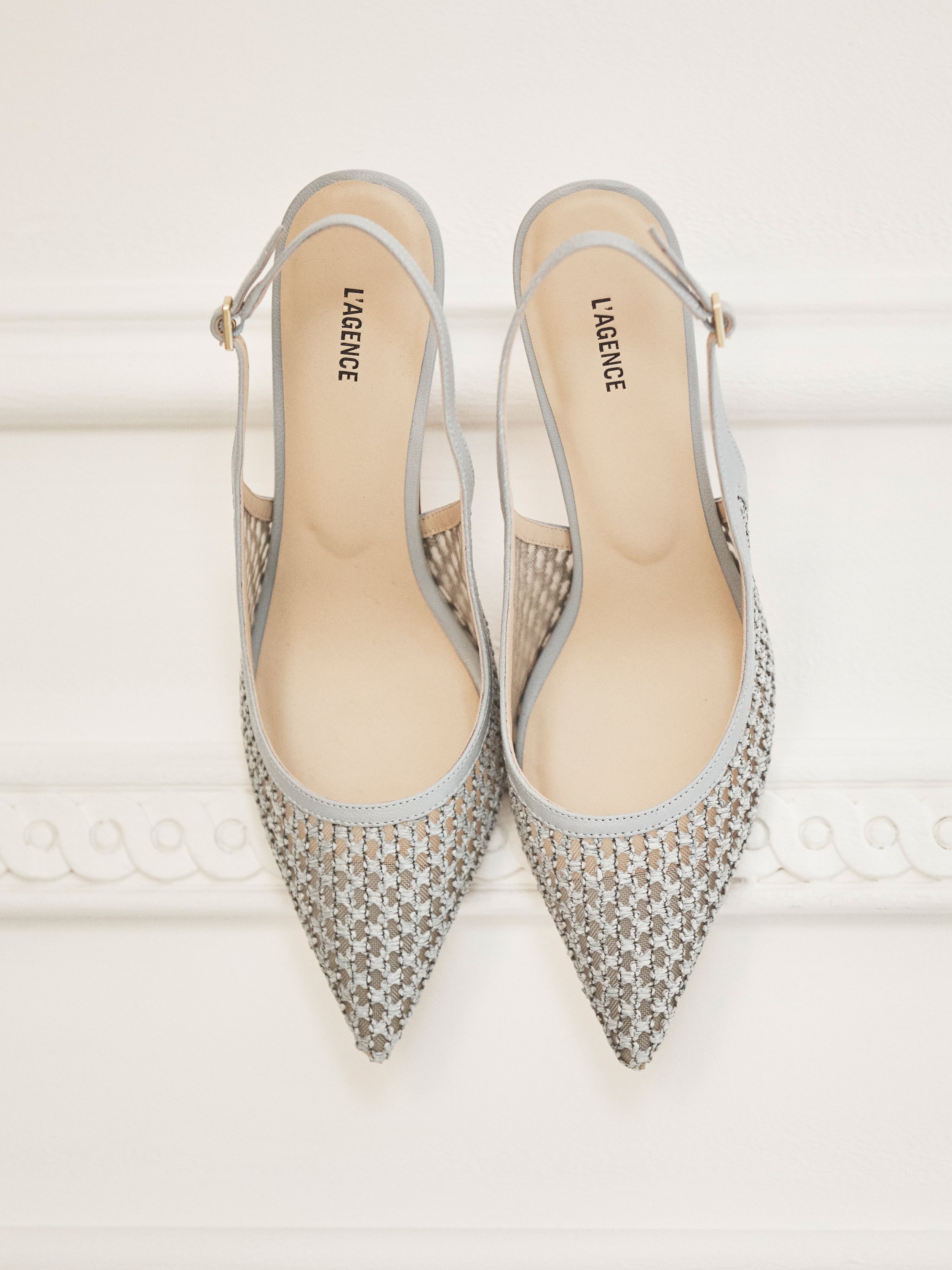 A pair of stylish, pointed-toe slingback shoes with a woven pattern in light grey and beige, featuring an elegant silhouette, displayed side by side against a white background.