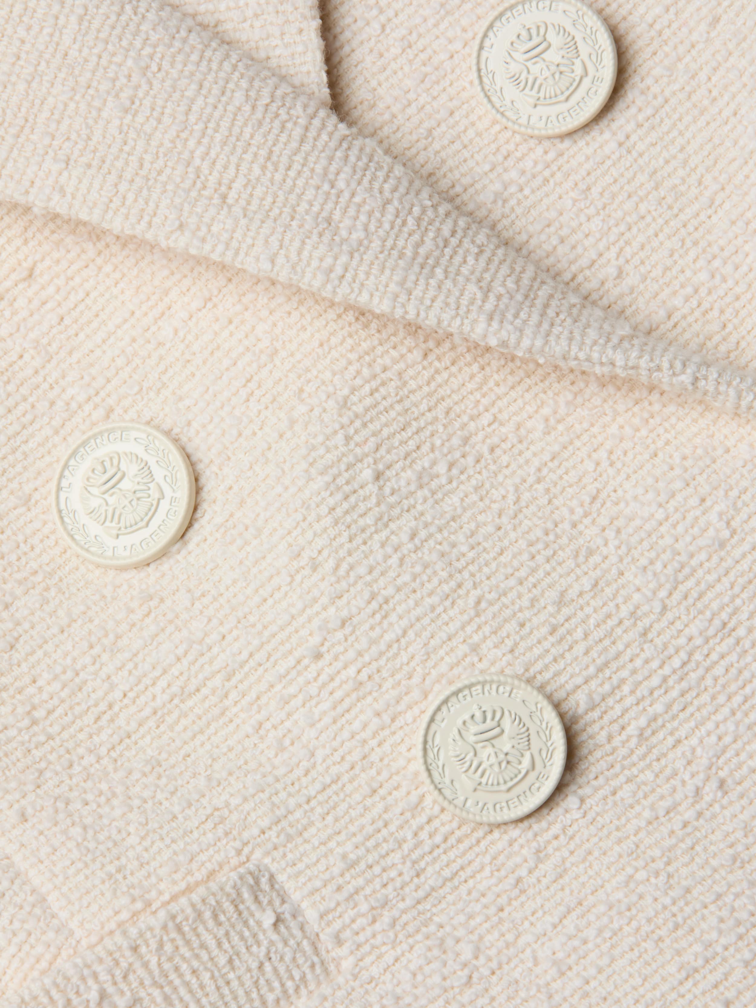 Close-up of the cream-colored, textured fabric from the Brooke Tweed Blazer, showcasing four embossed round buttons adorned with a laurel wreath and crest design.