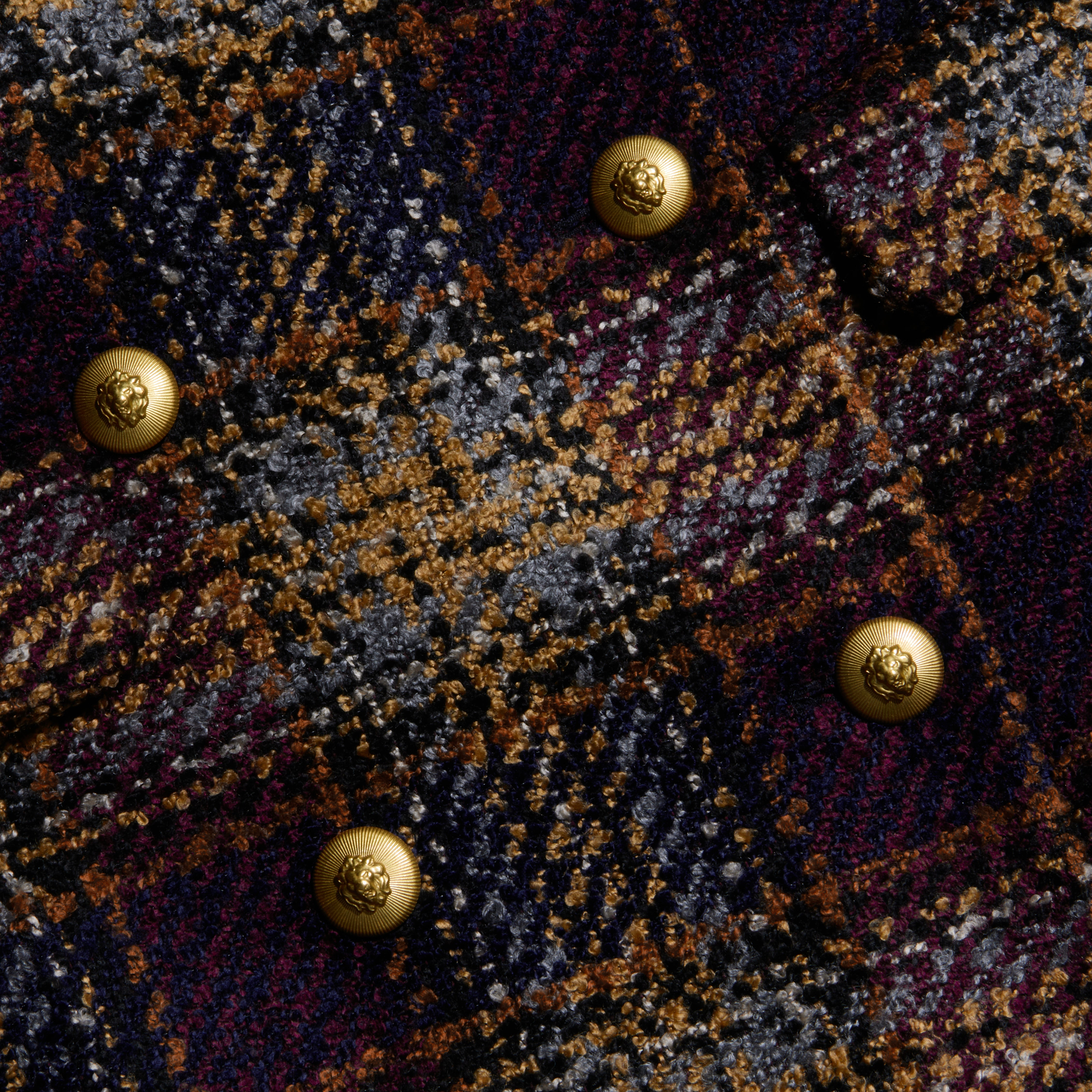 Close-up of the Kolina Tweed Long Coat’s textured plaid fabric in dark blue, brown, and gold tones, featuring six shiny round gold buttons arranged in two columns.