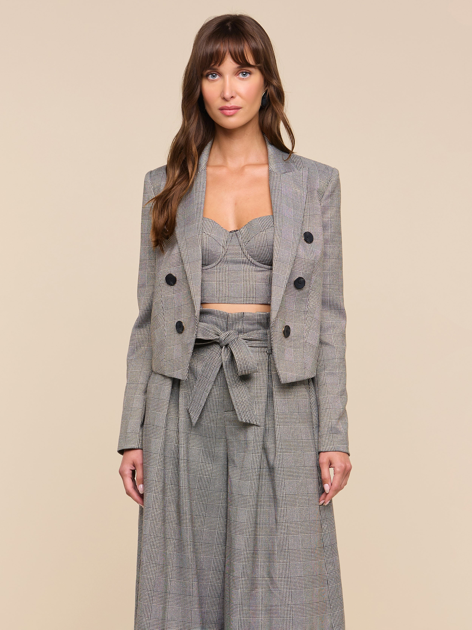 A woman stands facing forward, wearing the Lila Tweed Blazer styled with a crop top and high-waisted wide-leg pants featuring a bow tie at the waist, set against a plain light background.