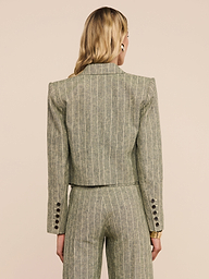 A person with long blonde hair is shown from behind, wearing the Lila Linen-Blend Blazer in a pinstriped olive green design with matching trousers. The suit features button details on the cuffs and offers a refined, fitted silhouette.